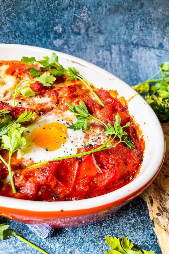 Vegetarian Shakshuka is served on the blue table with parsley and bread #eggs #red onion | hurrythefoodup.com